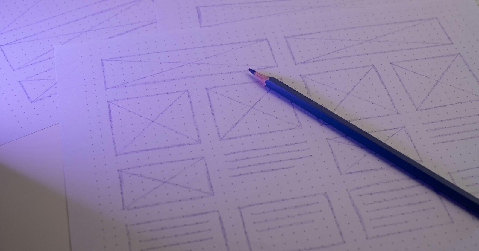 A pencil resting on hand-drawn wireframe sketches